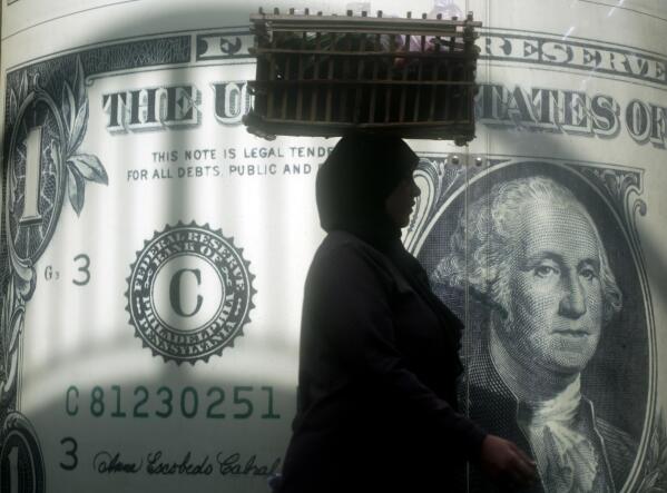 FILE - An Egyptian vendor walks past a poster showing a U.S. dollar outside an exchange office in Cairo, Egypt, Wednesday, Nov. 9, 2016. Egypt’s central bank has announced that it raised interest rates by 2% and switched to a more flexible exchange rate system. The institution said Thursday, Oct. 27, 2022 it had raised the lending rate, the deposit rate and the discount rate. (AP Photo/Amr Nabil, File)