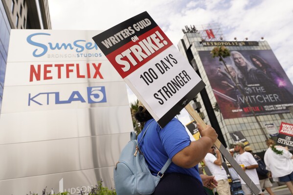 A picketer carries a sign outside Netflix studios on Wednesday, Aug. 9, 2023, in Los Angeles. The Hollywood writers strike reached the 100-day mark today as the U.S. film and television industries remain paralyzed by dual actors and screenwriters strikes. (AP Photo/Chris Pizzello)