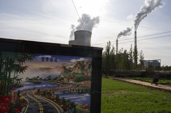 A resident rides past the Guohua Power Station in Dingzhou, Baoding in the northern China's Hebei province, Friday, Nov. 10, 2023. China and the U.S. have pledged to accelerate their efforts to address climate change ahead of a major U.N. meeting on the issue, making a commitment to take steps to reduce emissions of methane and other greenhouse gases besides carbon dioxide. (AP Photo/Ng Han Guan)