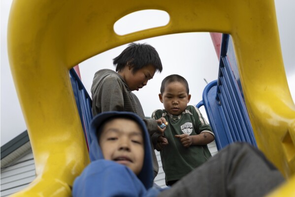 Wilson Noatak, 5, watches as Roy Nick lights a firework beside Joseph Phillip, 10, at a playground, Saturday, Aug. 19, 2023, in Akiachak, Alaska. Small firecrackers are for sale without age restriction from the Akiachak Enterprises general store. (AP Photo/Tom Brenner)