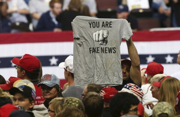 
              FILE - In this Oct. 4, 2018 file photo, a Trump supporter holds up a T-shirt reading "You Are Fake News" before a rally by President Donald Trump in Rochester, Minn. Local members of the media says they’ve noticed more hostility from the public since Trump began his attacks on ‘fake news.’ Trade groups are spreading safety tips because of the incidents. (AP Photo/Jim Mone, File)
            