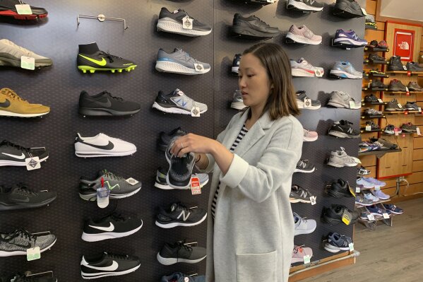 In this photo taken Wednesday, Aug. 28, 2019, Jennifer Lee, whose family owns Footprint shoe store in San Francisco, stands by a wall of athletic shoes, many of which are made in China and will be subject to new U.S. tariffs on Chinese goods starting Sept 1. (AP Photo/Terry Chea)