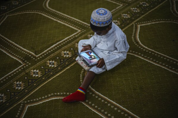 A Muslim boy engages with his tablet at the mosque after prayer, in Havana, Cuba, Friday, Feb. 16, 2024. The only mosque in Havana opened in 2015 and the Muslim community has grown to about 2,500 people nationwide. (AP Photo/Ramon Espinosa)