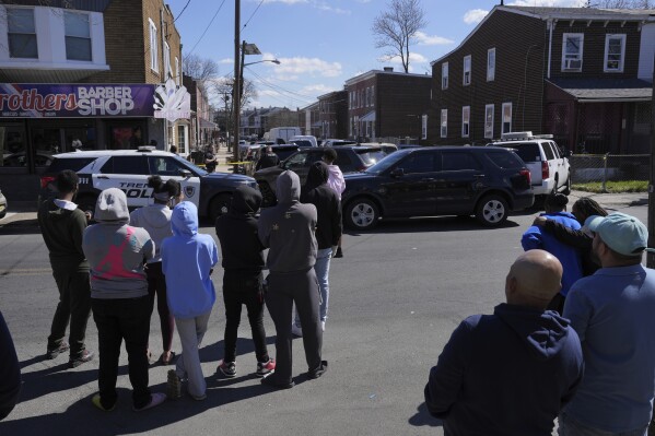 People look on as police surround a home in Trenton, N.J., Saturday, March 16, 2024. A suspect has barricaded himself in the home and was holding hostages after shooting three people to death in suburban Philadelphia. (AP Photo/Matt Rourke) (AP Photo/Matt Rourke)