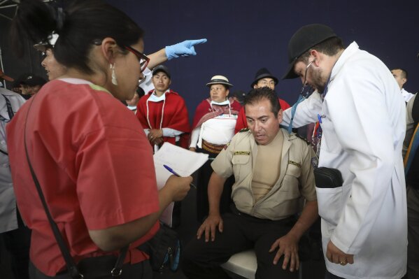 Doctors check the vitals of Col. Cristian Rueda Ramos, one of several police officers who has been detained by anti-government protesters, on a stage at the Casa de Cultura in Quito, Ecuador, Thursday, Oct. 10, 2019. An indigenous leader and four other people have died in unrest in Ecuador since last week, the public defender's office said Thursday. (AP Photo/Fernando Vergara)