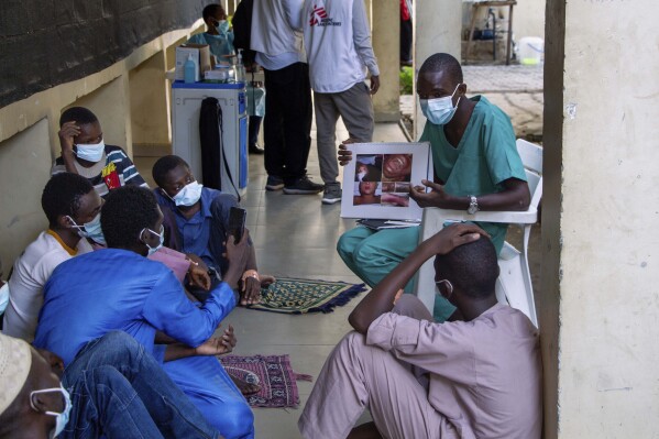 In this handout photo released by MSF, a health worker educating a group of male patients and care givers on the symptoms of Diphtheria at the Murtala muhammad specialist hospital in Kano, Nigeria Monday, Aug. 21, 2023. Authorities in several West African countries are trying to manage their huge diphtheria outbreaks, including in Nigeria where a top health official said Thursday Nov. 23, 2023 that millions are being vaccinated to cover wide gaps in immunity against the disease. (Ehab Zawati, MSF via AP)