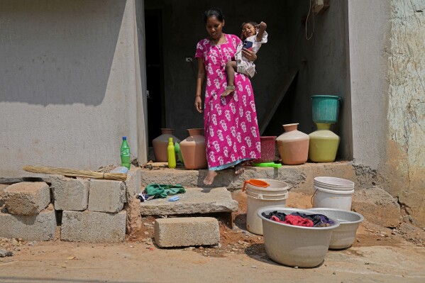 A resident of Ambedkar Nagar, a low-income settlement in the shadows of global software companies in Whitefield neighborhood, walks past the empty water cans outside her house in Bengaluru, India, Monday, March 11, 2024. Bengaluru is witnessing an unusually hot February and March, and in the last few years, it’s received little rainfall in part due to human-caused climate change. (AP Photo/Aijaz Rahi)