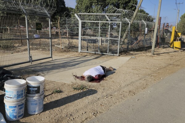 The body of a man shot dead lies in front of a gate at Kibbutz Kfar Azza during an attack by Hamas militants from the Gaza Strip, Saturday, Oct. 7, 2023. (AP Photo/Hassan Eslaiah)