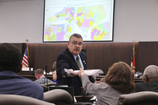 FILE - A sergeant-at-arms in the North Carolina state Senate passes out copies of a map proposal for new state Senate districts during a committee hearing at the Legislative Office Building in Raleigh, N.C., Thursday, Oct. 19, 2023. A federal lawsuit filed Monday, Nov. 20, 2023, in North Carolina alleges newly adopted district boundaries for the state Senate divide a cluster of predominantly Black counties in the northeast corner of the state in a way that will unfairly dilute the voting power of Black residents. (AP Photo/Hannah Schoenbaum, File)