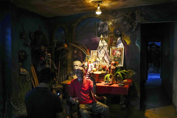 FILE - Juan Gonzalez sits next to his altar adorned Santeria and Catholic deities along with a photo of the late Cuban leader Fidel Castro, at his home in El Cobre, Cuba, Feb. 10, 2024. Diverse beliefs can be found mixed together on altars in Cuban homes, with the Virgin Mary sharing space with a ceramic Buddha and a warrior spirit from the Afro-Cuban faith. (AP Photo/Ramon Espinosa, File)
