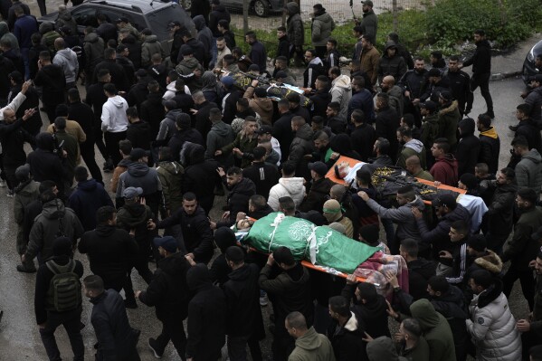 Palestinian gunmen march with bodies of militants draped in the Hamas militant group flag, left, and Palestinian Islamic Jihad, right, killed in an Israeli military raid at Ibn Sina Hospital in the West Bank town of Jenin, Tuesday, Jan. 30, 2024. (AP Photo/Majdi Mohammed)