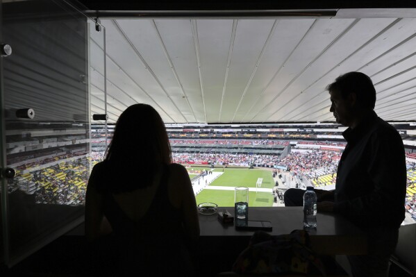 Roberto Ruano, the secretary of an association of box owners, right, and his partner Eve de la Torre, stand in their skybox for an interview during a Kings League Americas soccer game at Azteca Stadium in Mexico City, Saturday, May 4, 2024. FIFA asks host stadiums for the World Cups to relinquish full control of the building 30 days before the first match and seven days after the last one, including the boxes. (AP Photo/Ginnette Riquelme)