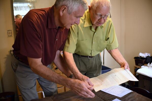 In this Saturday, July 17, 2021, photo, Dave Ware, left, and his father, Fred Ware, look over a deed and copy of a covenant for their home in Manchester, Conn. Fred and Dave Ware recently found a whites-only covenant on his property dating back to 1942 when researching the title chain. Upon finding the covenant, Dave Ware, who grew up in the home, reached out to state lawmakers and helped get a bill passed that strips these covenants on properties. (AP Photo/Jessica Hill)