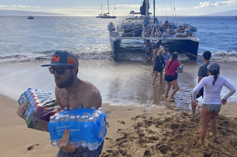 A group of volunteers who sailed from Maalaea Bay, Maui, form an assembly line on Kaanapali Beach on Saturday, Aug. 12, 2023, to unload donations from a boat. Maui residents have come together to donate water, food and other essential supplies to people on the western side of the island after a deadly fire destroyed hundreds of homes and left scores of people homeless. (AP Photo/Rick Bowmer)