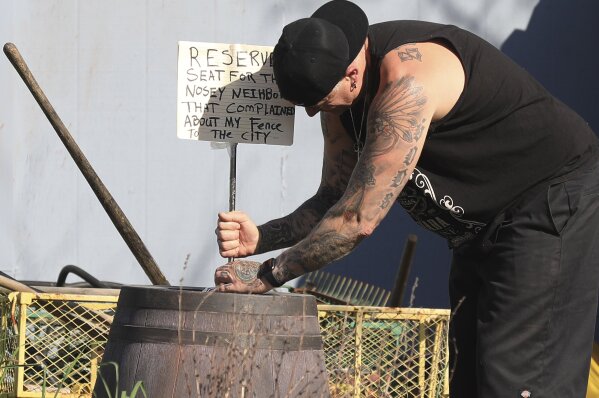 
              In this Monday, March 18, 2019 photo, homeowner Jason Winduce attempts to keep a sign he wrote from tipping over in the wind after he set up a display of nude mannequins in his Santa Rosa, Calif., yard, stemming from a neighbor's complaint to the city that a six foot-tall fence was a code violation. Winduce had to cut the fence to thee feet. (Kent Porter/The Press Democrat via AP)
            