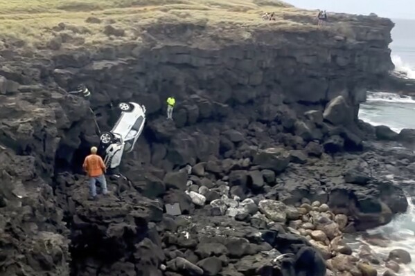In this image taken from video provided by Mike Moody, people work to tow a Jeep to safety after it was accidentally driven off a cliff in Naalehu, Hawaii, on Sunday, Feb. 25, 2024. A tourist driving in the early-morning dark on the southern tip of Hawaii's Big Island accidentally drove the rented Jeep off the cliff, but was able to swim to shore until firefighters pulled him up with a rope and helicopter. (Mike Moody via AP)