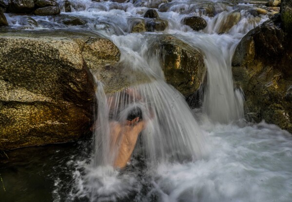 A Kashmiri man cools off at a stream on a hot summer day on the outskirts of Srinagar, Indian controlled Kashmir, Tuesday, July 4, 2023. (AP Photo/Mukhtar Khan)
