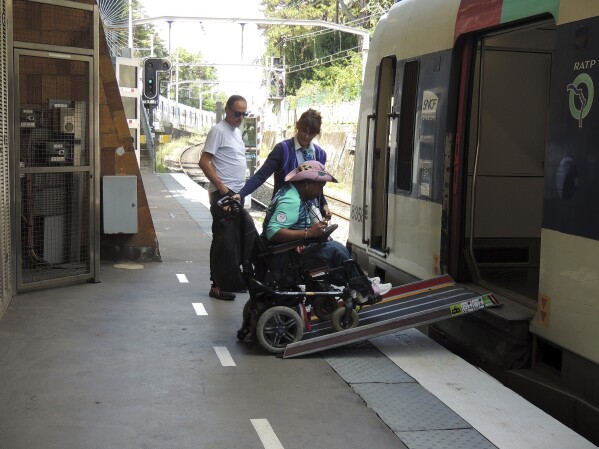 Ndieme Lame, a 57-year-old volunteer for the Paris 2024 Olympic and Paralympic Games navigates a ramp to join a RER train with the help of rail agents, during the 2024 Summer Olympics, Wednesday, Aug. 7 2024, in Paris, France. (AP Photo/Tom Nouvian)