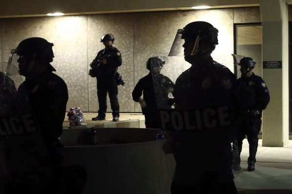 FILE - Phoenix Police stand in front of police headquarters on May 30, 2020, in Phoenix, waiting for protesters marching to protest the death of George Floyd. Phoenix police violate people’s rights, discriminate against Black, Hispanic and Native American people when enforcing the law and use excessive force, including unjustified deadly force, the U.S. Justice Department said Thursday, June 13, 2024. (AP Photo/Ross D. Franklin, File)