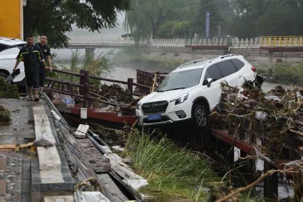 Residents walk near a vehicle washed away by floodwaters in the Mentougou district on the outskirts of Beijing, Tuesday, Aug. 1, 2023. Chinese state media report some have died and others are missing amid flooding in the mountains surrounding the capital Beijing. (AP Photo/Ng Han Guan)