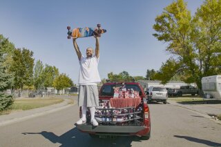 This Oct. 6, 2020 photo released by Ocean Spray shows  Nathan Apodaca holding his skateboard while standing in the back of a truck with Ocean Spray products in Idaho Falls, Idaho. Apodaca is enjoying fame from a 22-second TikTok video in which he chugs cranberry juice and sings along to Fleetwood Mac’s “Dreams” while cruising down an Idaho highway atop a longboard. The video has racked up 28 million views and counting since he posted it last month. Ocean Spray, whose juice Apodaca is seen swigging in the video, gave him a new truck stocked with juice this week. (Wesley White/Ocean Spray via AP)