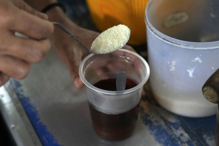 An employee puts a spoon of sugar into a cup of coffee as he serves a customer at a food stall in Jakarta, Indonesia Tuesday, Oct. 24, 2023. Indonesia — the biggest sugar importer last year, according to the United States Department of Agriculture — has cut back on imports. (AP Photo/Tatan Syuflana)