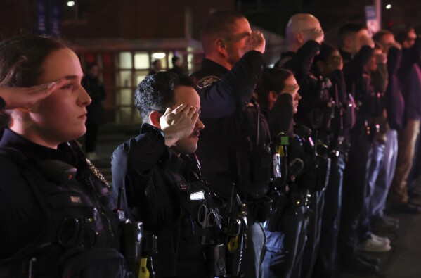 Police officers salute as the bodies of two officers are transported to the Wally Howard Forensics Science Center in Syracuse, N.Y., Monday, April 15, 2024. Police officers from several local agencies gathered at Upstate hospital's emergency room to hear the news of the slain officers. (Dennis Nett/The Post-Standard via AP)