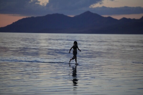 A young person runs through the Great Salt Lake on June 15, 2023, near Magna, Utah. People are rejoicing after the winter's snow melted and increased the lake's elevation beyond last year's record low. (AP Photo/Rick Bowmer)
