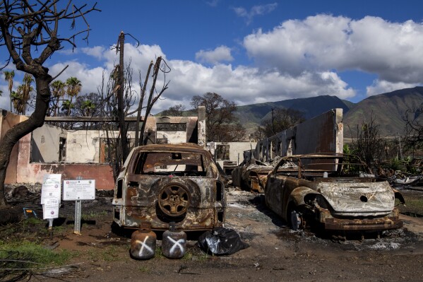 FILE - Burned cars and propane tanks with markings on them sit outside a house destroyed by wildfire, Friday, Dec. 8, 2023, in Lahaina, Hawaii. An acute housing shortage hitting fire survivors on the Hawaiian island of Maui is squeezing out residents even as they try to overcome the loss of loved ones, their homes and their community. (AP Photo/Lindsey Wasson, File)