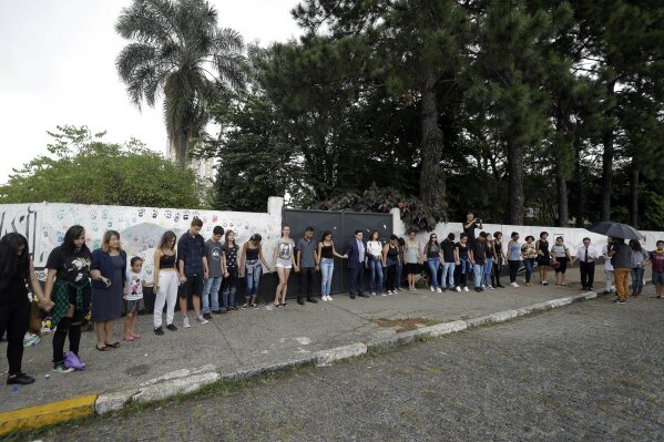 
              Students, relatives and neighborhood residents, pray outside the Raul Brasil State School one day after a mass shooting, in Suzano, Brazil, Thursday, March 14, 2019. Classmates, friends and families began saying goodbye on Thursday, with thousands attending a wake in the Sao Paulo suburb while authorities worked to understand what drove two former students to attack the school with a gun, crossbows and small axes. (AP Photo/Andre Penner)
            