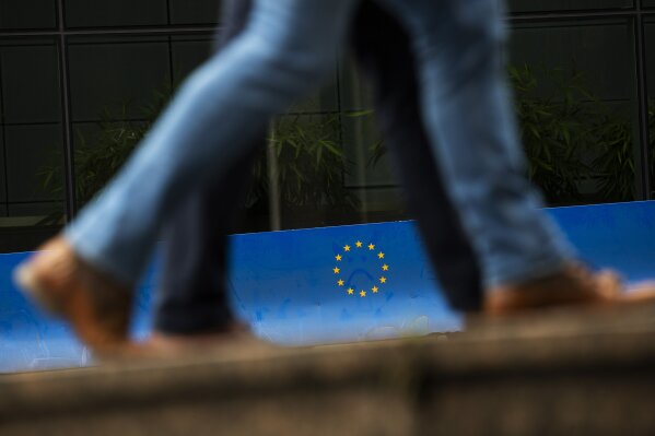 People walk past a European Union logo in a security fence at the European quarter in Brussels, Monday, Oct. 7, 2019. The British government insists that the country will leave the EU on Oct. 31 with or without a deal. (AP Photo/Francisco Seco)