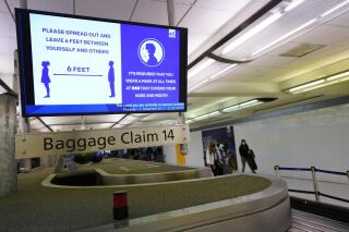 FILE - In this Dec. 10, 2020, file photo, an electronic sign warns travelers to maintain social distance in the terminal of Denver International Airport in Denver. About one-fifth of flight attendants say they've gotten into a physical incident with a passenger this year. That's according to a survey by their union. The Association of Flight Attendants says it wants people who act up during flights to face criminal prosecution — not just fines. Airlines have reported more than 3,600 cases of unruly passengers this year. Disputes over face masks are the most common trigger. Federal rules require face masks on planes until mid-Sept (AP Photo/David Zalubowski, File)