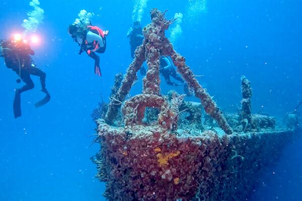 In this Sunday, May 15, 2022, photo provided by the Florida Keys News Bureau, divers swim near the bow of the retired Naval Landing Ship Dock Spiegel Grove, sunk 20 years earlier, six miles off Key Largo, Fla., to become an artificial reef. The vessel's storied past is to be celebrated May 17, 2022, the 20th anniversary of the sinking, with an event at a local cultural center that features key individuals reminiscing about the project. (Frazier Nivens/Florida Keys News Bureau via AP)