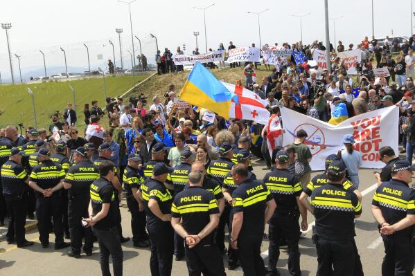 Georgian opposition activists with Georgian and Ukrainian national flags attend a protest against the resumption of air links with Russia standing behind a police line at the International Airport outside Tbilisi, Georgia, Friday, May 19, 2023. Direct flights resumed on Friday between Russia and Georgia amid protests and sharp criticism from the South Caucasus nation's president, just over a week after the Kremlin unexpectedly lifted a four-year-old ban despite rocky relations. (AP Photo/Shakh Aivazov)