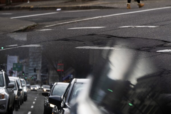 In this image taken through the reflection of a car window, a person walks along W Burnside Street near a repaired patch in the road on Thursday, Feb. 6, 2025, in Portland, Ore. (AP Photo/Jenny Kane)