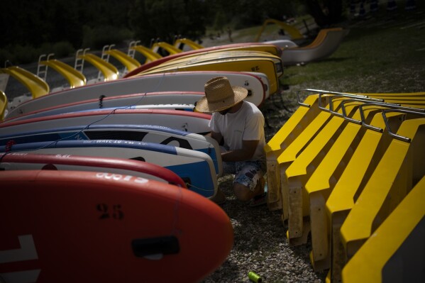 A worker prepares aquatic equipment for rental at the Lac de Castillon in southern France, Tuesday, June 20, 2023. Human-caused climate change is lengthening droughts in southern France, meaning the reservoirs are increasingly drained to lower levels to maintain the power generation and water supply needed for nearby towns and cities. It's concerning those in the tourism industry, who are working out how to keep their lakeside businesses afloat. (AP Photo/Daniel Cole)