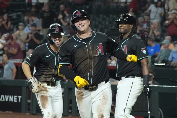 Arizona Diamondbacks' Joc Pederson, center, smiles as he celebrates with Corbin Carroll, left, and Josh Bell, right, after hitting a two-run double and scoring on a two-base error during the first inning of a baseball game, Wednesday, Aug. 14, 2024, in Phoenix. (AP Photo/Ross D. Franklin)