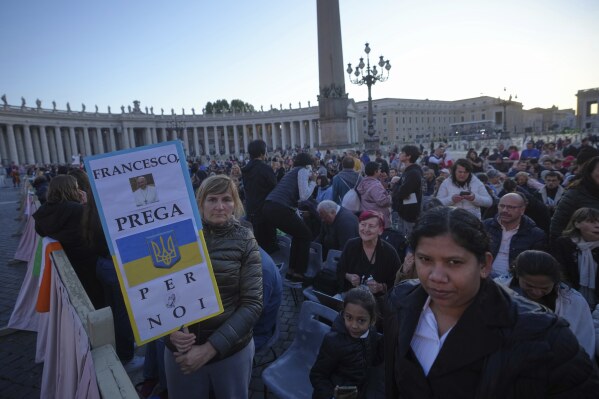 Faithful, one holding a placard with the Ukrainian flag and reading Francis, pray for us, arrive for the funeral of Pope Francis in St. Peter's Square at the Vatican, Saturday, April 26, 2025. (AP Photo/Alessandra Tarantino)