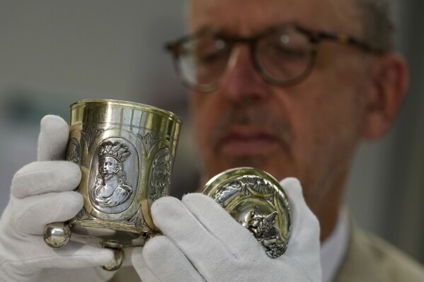 Matthias Weniger, curator of the Bavarian National Museum, lifts one of the 111 silver objects stolen by the Nazis from the Jews during the Third Reich, in Munich, Germany, Saturday, June 10, 2023. Museum staff have made it their mission to return as many of the silver objects as possible to the descendants of the original owners. (AP Photo/Matthias Schrader)
