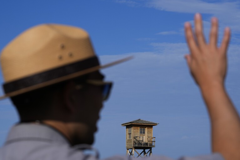 A reconstructed guard tower looms at the site's entrance as Kurt Ikeda, Director of Interpretation and Education at Minidoka National Historic Site, leads a tour for pilgrimage attendees Saturday, July 8, 2023, in Jerome, Idaho. (AP Photo/Lindsey Wasson)