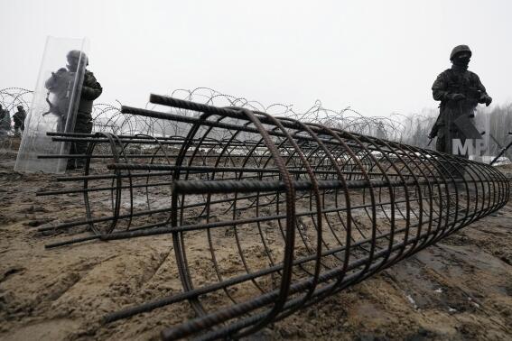 FILE - Guards and the military watching the start of work on the first part of a 180 kilometers (115 miles) and 5.5 meter (18ft)-high metal wall intended to block migrants from Belarus crossing illegally into EU territory, in Tolcze, near Kuznica, Poland, Jan. 27, 2022. When relations with Belarus deteriorated after its authoritarian President Alexander Lukashenko was declared the winner of an election widely seen as fraudulent, the government in Minsk sent thousands of migrants streaming across the EU's frontiers. In response, Poland and Lithuania erected walls along their borders with Belarus. (AP Photo/Czarek Sokolowski, File)