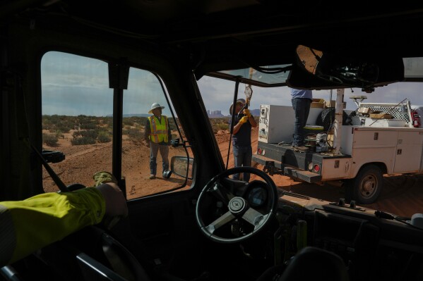 CORRECTS LAST NAME TO ATENE FROM BLACK - Robert Atene, left, with the Navajo Tribal Utility Authority, supervises as a volunteer crew lifts a power line pole, Tuesday, Oct. 8, 2024, on the Navajo Nation in Halchita, Utah. (AP Photo/Joshua A. Bickel)