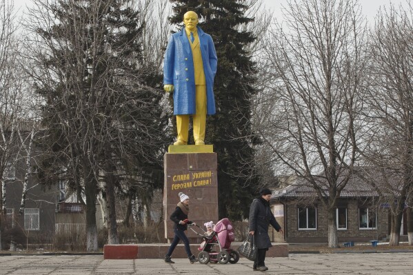  People walk by a statue of Vladimir Lenin, painted in the colors of Ukraine's national flag, in Velyka Novosilka, Ukraine, on Thursday, Feb. 19, 2015.  (AP Photo/Vadim Ghirda, File)