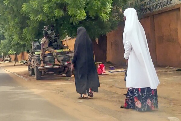 In this image taken from video, two women walk past soldiers in Niamey, Niger, Friday, July 28, 2023. The general who led a coup in Niger defended the takeover on state television and called for support. of the nation and international partners, as concerns grew that the political crisis could set back the country's fight against jihadists and increase Russia's influence in West Africa.  (AP Photo)