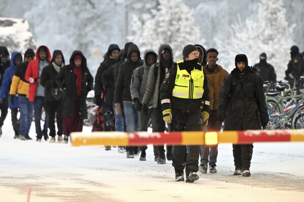 Finnish Border Guards escort migrants at the international border crossing between Finland and Russia, in Salla, Finland, Thursday, Nov. 23, 2023. (Jussi Nukari/Lehtikuva via AP)