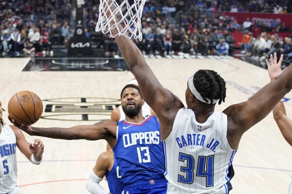 Los Angeles Clippers forward Paul George, left, shoots as Orlando Magic center Wendell Carter Jr. defends during the first half of an NBA basketball game Tuesday, Oct. 31, 2023, in Los Angeles. (AP Photo/Mark J. Terrill)