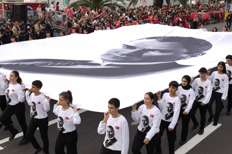 Youngsters hold a banner of Turkey's founding father Mustafa Kemal Ataturk as they take part in a parade during celebrations marking the 100th anniversary of the creation of the modern secular Turkish Republic, in Istanbul, Turkey, Sunday, Oct. 29, 2023. Turkey is marking its centennial but a brain drain is casting a shadow on the occasion. Government statistics indicate that a growing number of the young and educated are looking to move abroad in hopes of a better life, mainly in Europe. (AP Photo/Emrah Gurel)