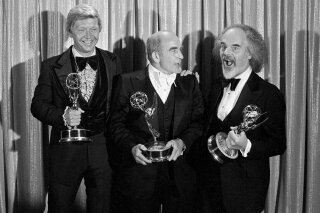 FILE - In this Sunday, Sept. 11, 1977 file photo, Screenwriter William Blinn, left, Ed Asner, center, and David Greene pose with their Emmy statuettes at the annual Primetime Emmy Awards presentation in Los Angeles. William Blinn, a screenwriter for the landmark TV projects “Brian’s Song”, “Roots” and the Prince film “Purple Rain,” has died, Thursday, Oct. 22, 2020. He was 83. (AP Photo/File)