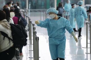 FILE - Workers wearing protective gear direct arriving passengers to quarantine hotels in the Hong Kong International Airport, Friday, April 1, 2022. Hong Kong’s government says its population has shrunk for a second year as anti-virus controls hampered the inflow of new workers and births declined, but it made no mention of an exodus of residents following a crackdown on a pro-democracy movement. (AP Photo/Kin Cheung, File)