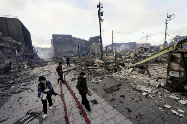 People walk past collapsed buildings following an earthquake in Wajima, Ishikawa prefecture, Japan Tuesday, Jan. 2, 2024. (Kyodo News via AP)